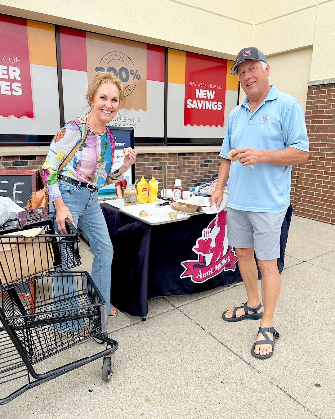 A man and a woman enjoy free brat and hot dog samples in front of a store.