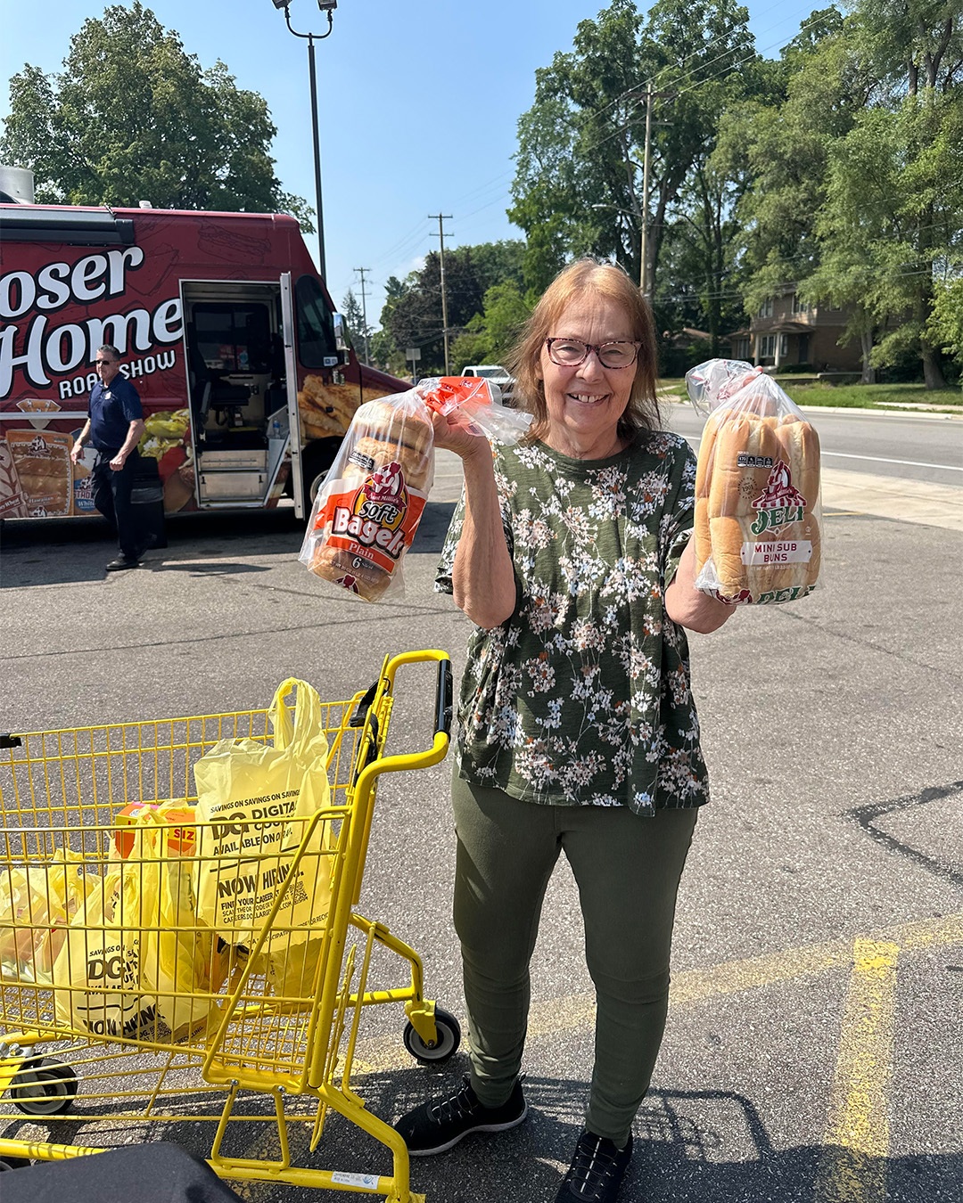A woman holds a bag of Aunt Millie's bagels and a bag of Aunt Millie's mini sub buns in a Dollar General parking lot on sunny day.